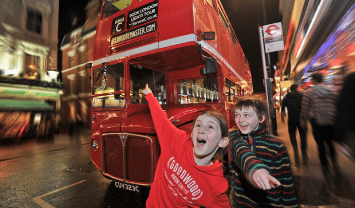 Two happy children standing infront of a redroutemaster.com bus at night