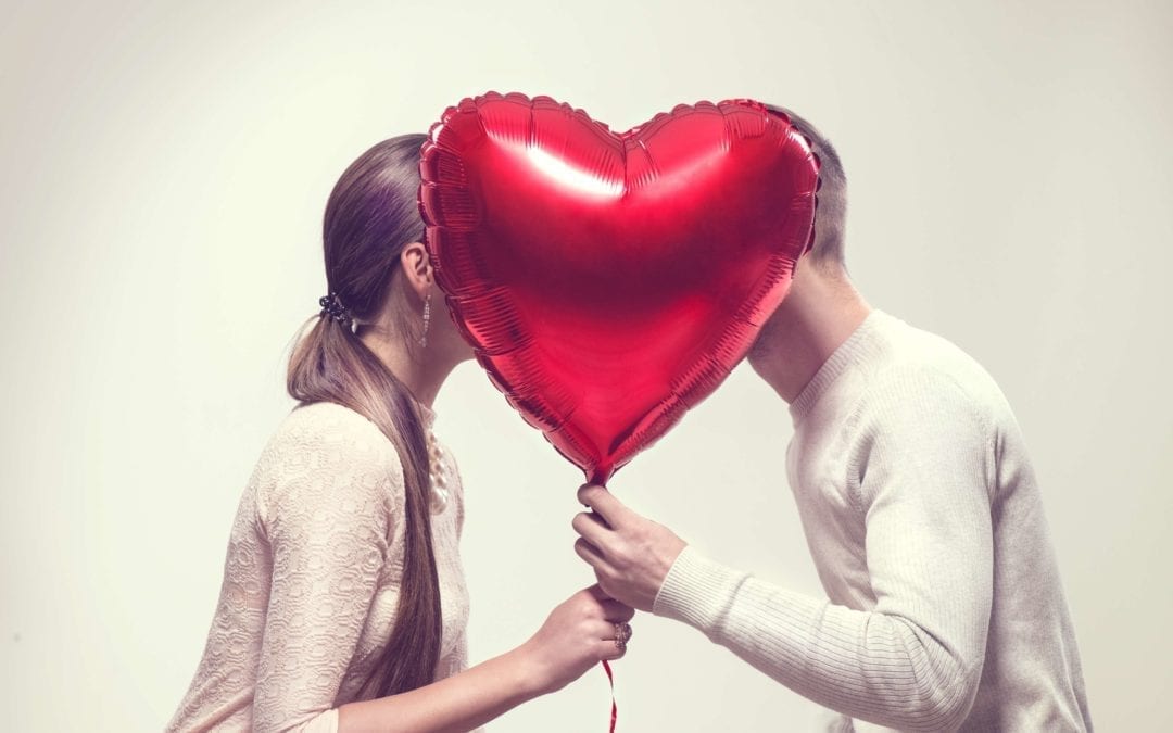 Two people looking at eachother behind a red heart shaped balloon