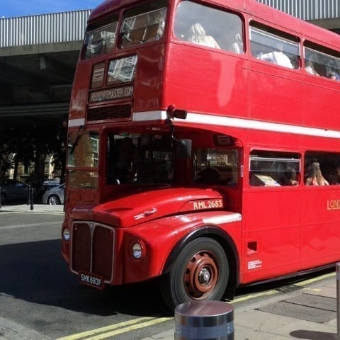 Routemaster bus full of people next to a bridge